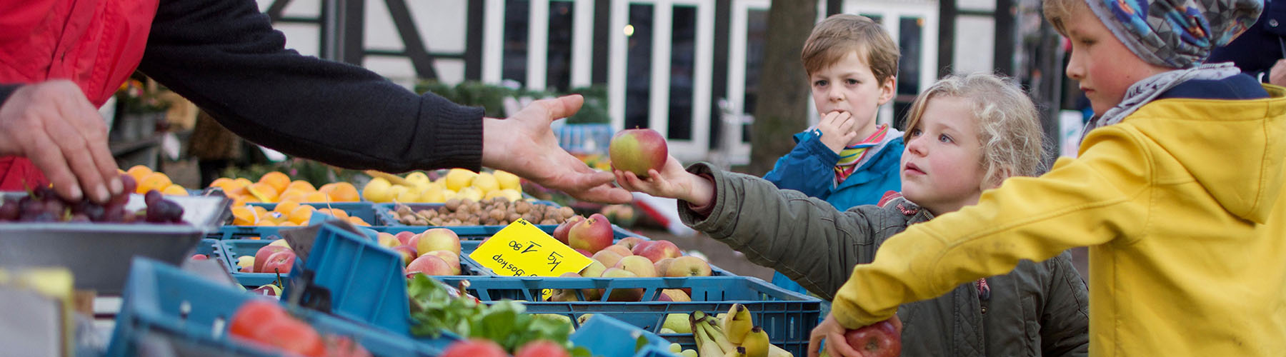 Mädchen erhält von einem Obst- und Gemüsehändler am Wochenmarkt einen Apfel