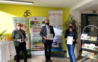Übergabe des "JOB & FIT-Zertifikats" im niedersächsischen Landwirtschaftsministerium. Abgebildet sind drei Personen vor Postern und einem Prospektständer.