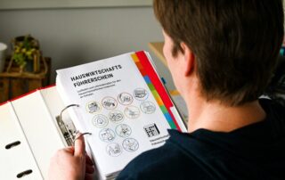 Eine Frau liest aus einem Aktenordner die Titelseite zum "Hauswirtschaftsführerschein"