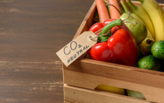 Mit Gemüse und Obst befüllte Holzkiste und einem Anhänger um eine Paprika mit der Aufschrift "CO2 Neutral"