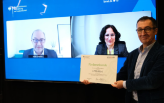 Übergabe einer Förderurkunde durch den Minister des BMEL. Im Hintergrund zwei per Webcam zugeschaltete Personen.