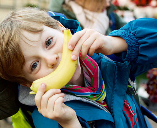Ein Kind, welches mit einer Banane vor dem Mund ein Lächeln zeigt