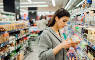 Junge Frau schaut auf die Zutatenliste einer Packung im Supermarkt