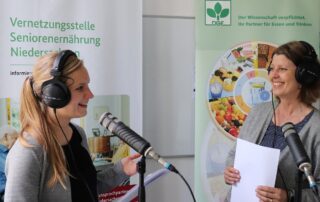 2 Frauen mit Kopfhörer und Mikrofon lächeln sich an