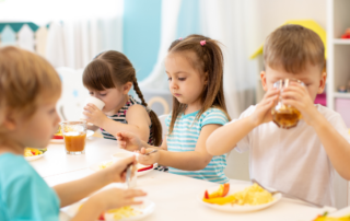 Kindergartenkinder an einem Tisch, die essen und trinken