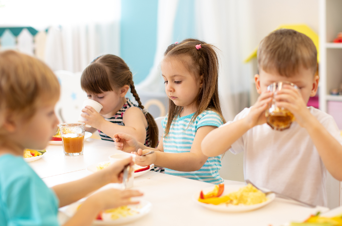 Kindergartenkinder an einem Tisch, die essen und trinken