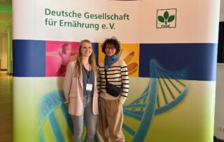 Zwei Mitarbeiterinnen der DGE Sektion Niedersachsen vor einem Aufsteller der DGE bei einer Veranstaltung